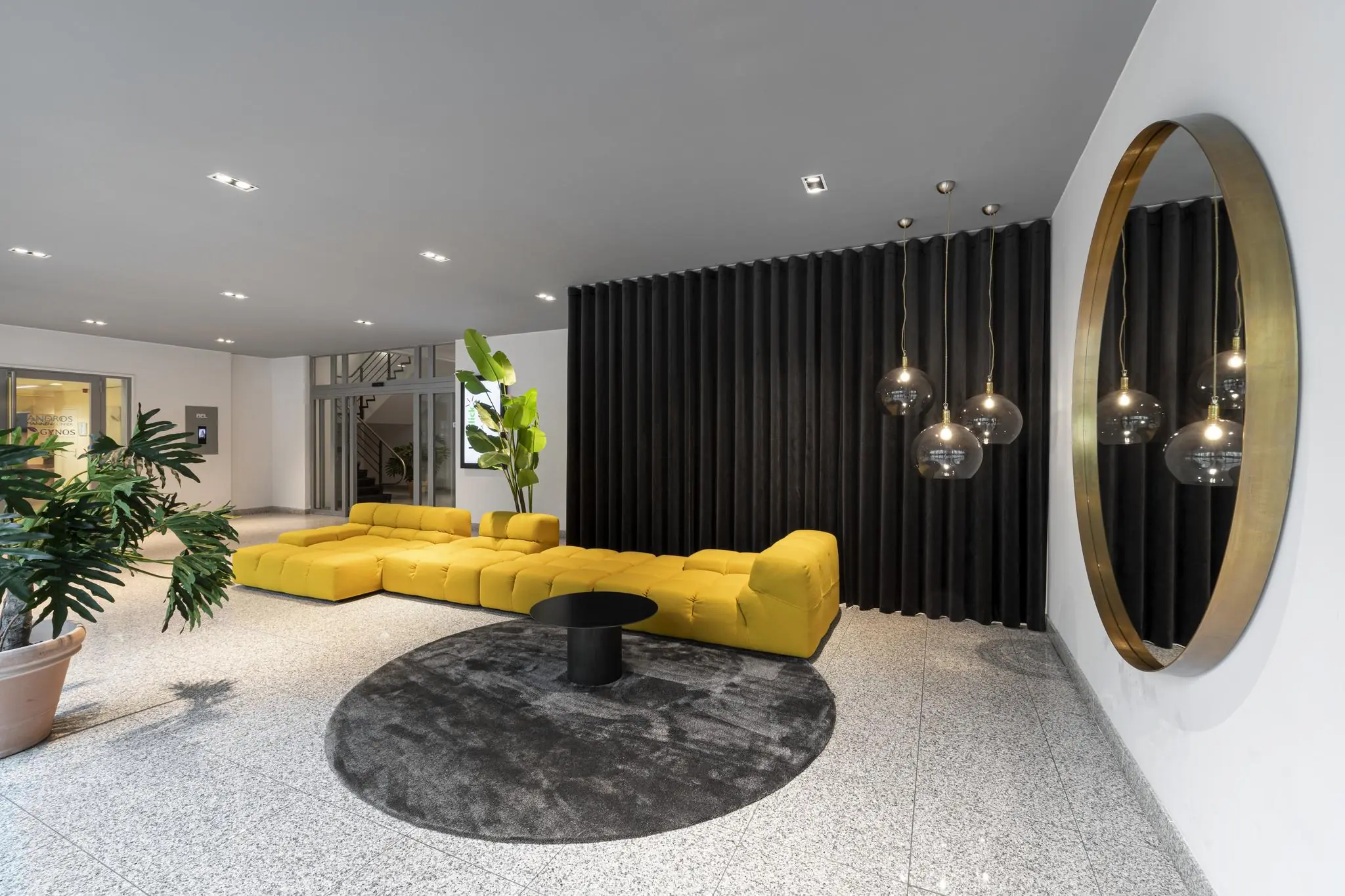 Moderne entreehal aan de Van Boshuizenstraat met een felgele loungebank, zwarte wandbekleding, hanglampen en een grote ronde spiegel.